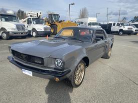 A 1966 Ford Mustang in gray with a black front grille and gold wheels, featuring a sleek body design and sporty appearance