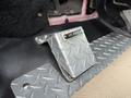 A metal air horn pedal with a diamond plate design located on the floor of a vehicle