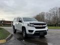 A 2019 Chevrolet Colorado in white with a dark hood and a utility cap on the bed parked on a street