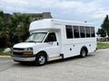A white 2015 Chevrolet Express bus with large windows and a high roof parked on a paved surface