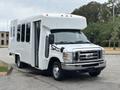 A white 2014 Ford E-350 with a boxy body design and large windows is parked with its doors open showcasing a spacious interior and a shiny chrome grille