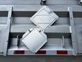 Close-up of a silver truck's rear door featuring two diamond-shaped access panels with latches and a red and white striped reflective tape below