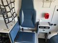 A blue driver's seat in a vehicle cabin with a control panel and storage compartment nearby