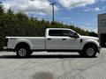 A white 2020 Ford F-350 Super Duty pickup truck with four doors and a long bed is parked on a gravel surface