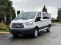 A white 2018 Ford Transit van with a sliding side door and silver wheels is parked at an angle showcasing its front grille and headlights
