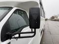 A 2011 Ford F-550 with a large side mirror and a white exterior showing raindrops on its surface