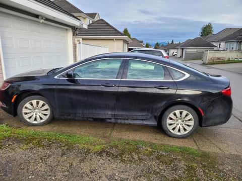 A black 2016 Chrysler 200 parked on a driveway with visible dirt on the side and white alloy wheels