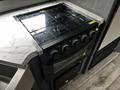 A black gas stove with five knobs and a glass top is installed in a camper's kitchen space