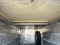 An empty metal truck bed with a mounted spare tire leaning against the side and a smooth ceiling above