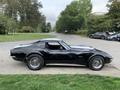 A 1972 black Chevrolet Corvette with a sleek body, distinctive curves, and classic silver wheels positioned on a street