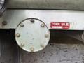 A metal panel with a round gauge featuring several bolts and a red label marked COMP. NO. and 7500 LITRES