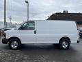 A white 2014 Chevrolet Express van with a sliding side door and chrome wheels is parked, showcasing its side profile and smooth body design