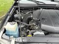 The image shows the engine compartment of a 2015 Toyota Tacoma with a V6 engine and various components including hoses and a coolant reservoir