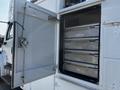 An open side door of a 2004 Freightliner M2 revealing multiple metal storage shelves inside the vehicle