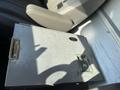A silver metal storage box with a lock sits on the floor of a vehicle next to a leather seat