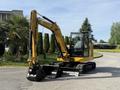 A 2022 Caterpillar 306 excavator with a yellow body and black tracks positioned on a path surrounded by greenery