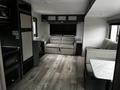 Interior of a 2022 Aspen Trail travel trailer featuring a light-colored sofa and seating area with wooden flooring and modern appliances