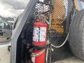A red fire extinguisher mounted on a vehicle frame with a metal rack and warning instructions visible on the label