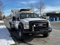 A white 2011 Ford F-450 Super Duty truck with a flatbed and amber warning lights on the roof parked on a snowy surface