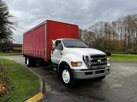 A white 2008 Ford F-750 truck with a red cargo box is parked, featuring a large front grille and a flatbed design with dual rear wheels