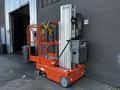 A 2000 JLG 12SP aerial work platform with an orange frame and extended lift arms standing beside a gray wall