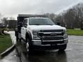 A white 2021 Ford F-550 Super Duty pickup truck with a black flatbed trailer attached