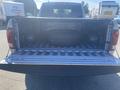 The image shows the open tailgate of a 2021 RAM 1500 revealing the truck bed with a spare tire and a textured floor surface