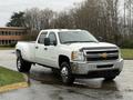 A white 2013 Chevrolet Silverado 3500HD pick-up truck with a crew cab and chrome accents is parked at an angle showcasing its front and side view