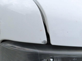 A close-up view of the front hood and headlight of a 2020 Chevrolet Express showing a gap in the hood and slight damage