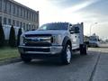 A 2018 Ford F-450 SD in a silver finish with a flatbed and two-tone wheels parked on a street