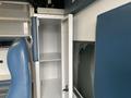 A white cabinet with a door open inside a Chevrolet Express showing empty shelves and blue seating nearby