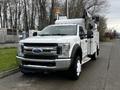 A 2018 Ford F-550 truck with a white exterior and an extended cab featuring equipment on top and storage compartments on the sides