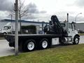 A 2006 Freightliner M2 112 flatbed truck with a mechanical arm attached on its rear side and a silver and black color scheme