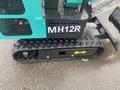 Close-up of a 2024 AGT Industrial MH12R Mini Excavator showing the tracked undercarriage with visible treads and a yellow directional arrow on the side