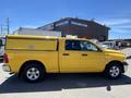 A yellow 2015 RAM 1500 pickup truck with a matching cap on the truck bed is parked in the foreground