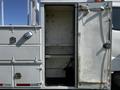 An open door of a 2004 Freightliner M2 revealing an empty storage compartment with metal shelves and hooks inside