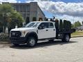 A white 2017 Ford F-550 with a flatbed and orange safety lights parked on a street