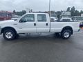 A white 2005 Ford F-350 SD pickup truck with a crew cab and a flatbed, featuring chrome wheels and side mirrors
