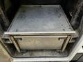 A metal storage compartment is open revealing a flat surface with a rectangular container underneath it inside a Ford F-550 vehicle