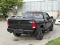 A black 2018 RAM 1500 pickup truck with a shiny exterior and off-road tires is parked, showcasing its rear view and dual exhaust pipe design