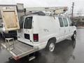 A white 2008 Ford Econoline van with a ladder rack and a lift attachment on the roof parked in a wet environment