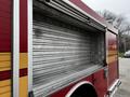 A 2009 Spartan Gladiator fire truck with a red exterior and yellow stripes featuring an open storage compartment showcasing metal shelving inside