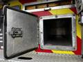 A metallic compartment door is open on a fire truck revealing an empty, rectangular storage space inside