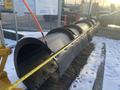 A large black plow with a 12-foot attachment featuring a curved design rests on snowy ground next to a measuring tape stretched across its length