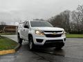 A white 2018 Chevrolet Colorado pickup truck with a cap on the bed is angled towards the viewer showcasing its front design and headlights