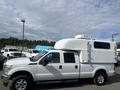 A 2014 Ford F-350 SD with a white camper shell mounted on its truck bed showcasing a streamlined design and large wheels