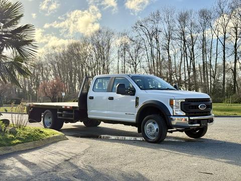 A white 2020 Ford F-550 with a flatbed design parked at an angle showcasing its large front grill and spacious cab