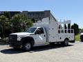 A white 2013 Ford F-550 flatbed truck with a tall, open-sided cargo area and a cab featuring orange lights on the roof