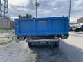 A blue 2009 Dodge Ram 5500 flatbed truck with a large dump bed labeled DORMEL parked on a gravel surface