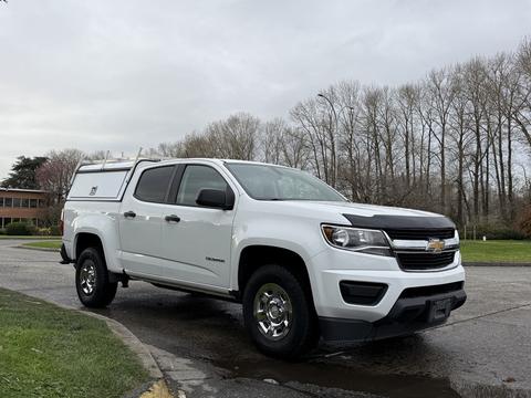 A white 2019 Chevrolet Colorado with a silver truck bed cap parked at an angle showcasing its front and side features